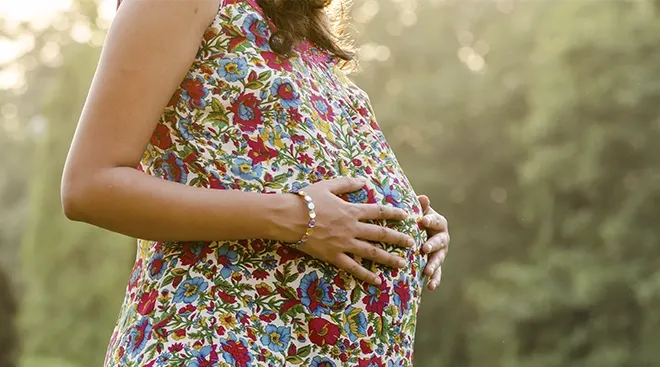 close up of pregnant woman wearing a floral dress outside in the summertime