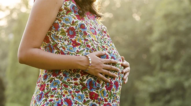 close up of pregnant woman wearing a floral dress outside in the summertime