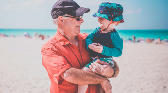 grandpa and toddler wearing hat for sun protection, on the beach