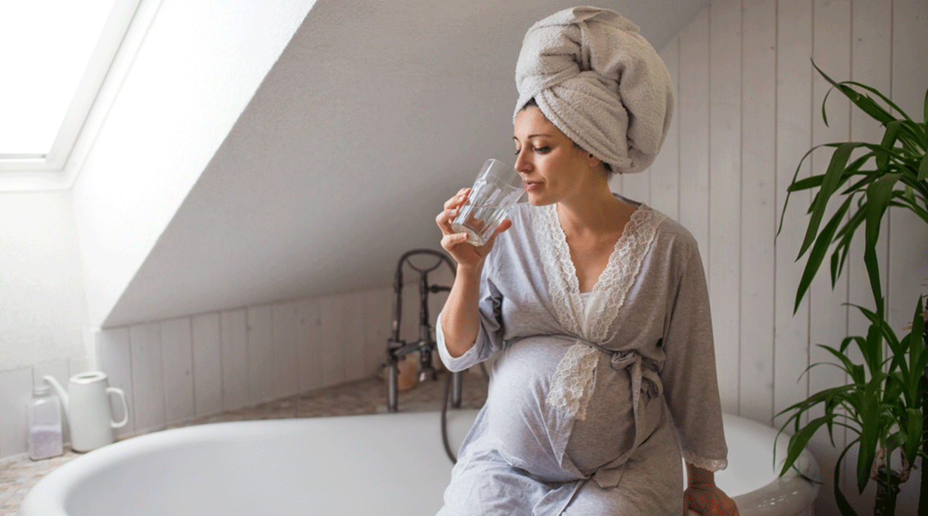 pregnant woman wearing a bath robe while sitting in bathroom