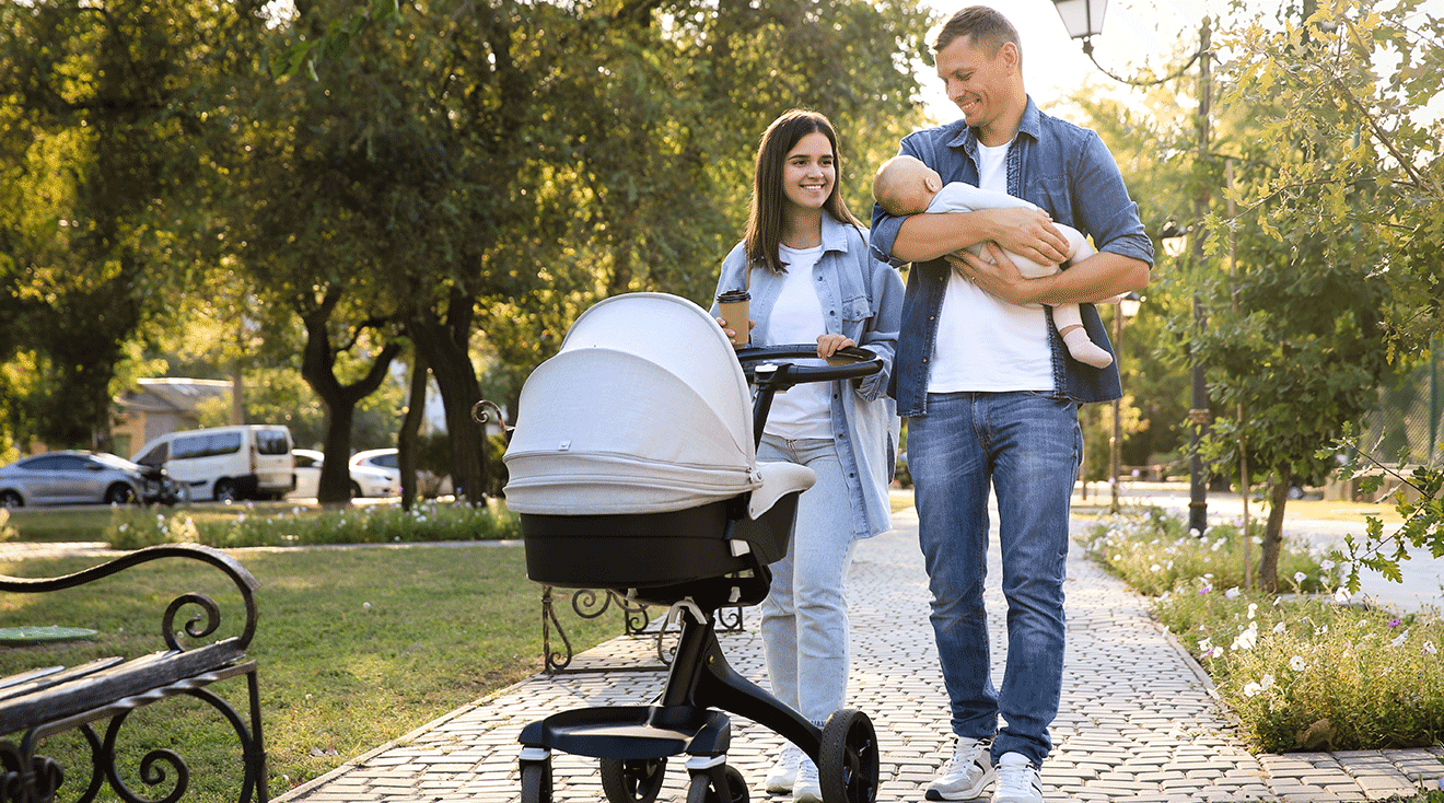 mom and dad walking with baby stroller through park