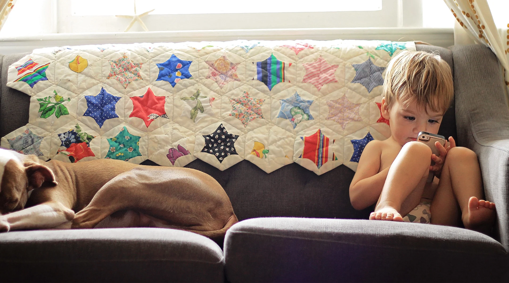 toddler boy sitting on coach at home staring at phone screen