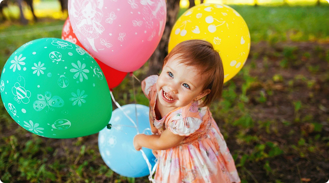 toddler girl with birthday balloons outside on a summer day