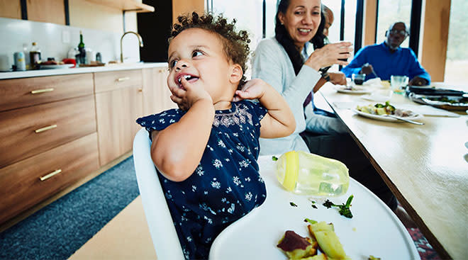 toddler eating in her high chair with family around