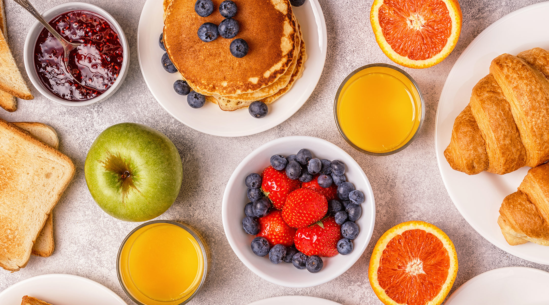 breakfast food spread including croissants, fruit, toast, and orange juice