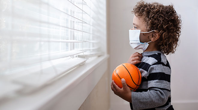 worried child looking out the window and holding a basketball