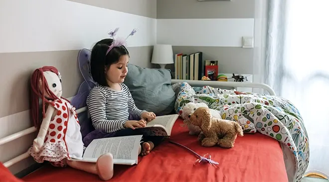 child reading a book and playing in her room with dolls
