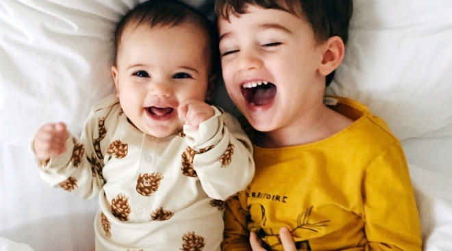 baby and big brother lay in bed laughing