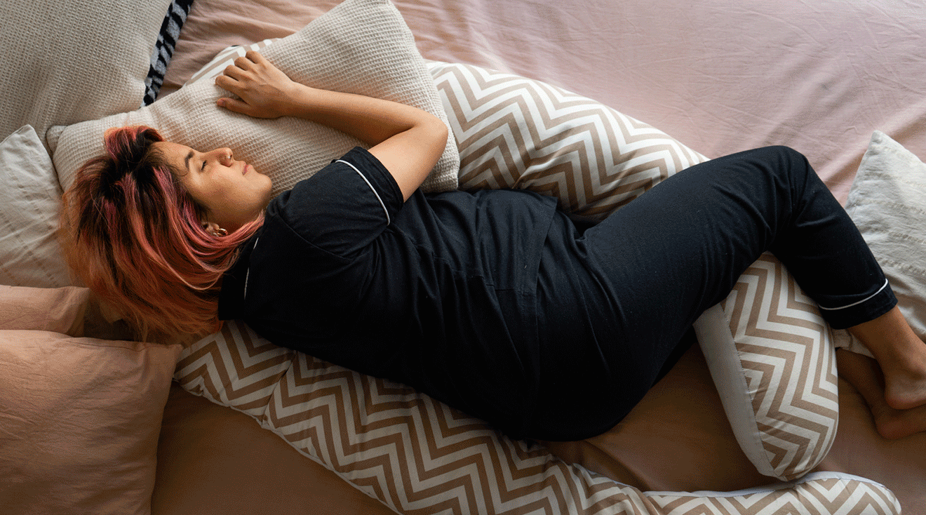 pregnant woman sleeping on side with pregnancy pillow, safe pregnancy sleeping positions