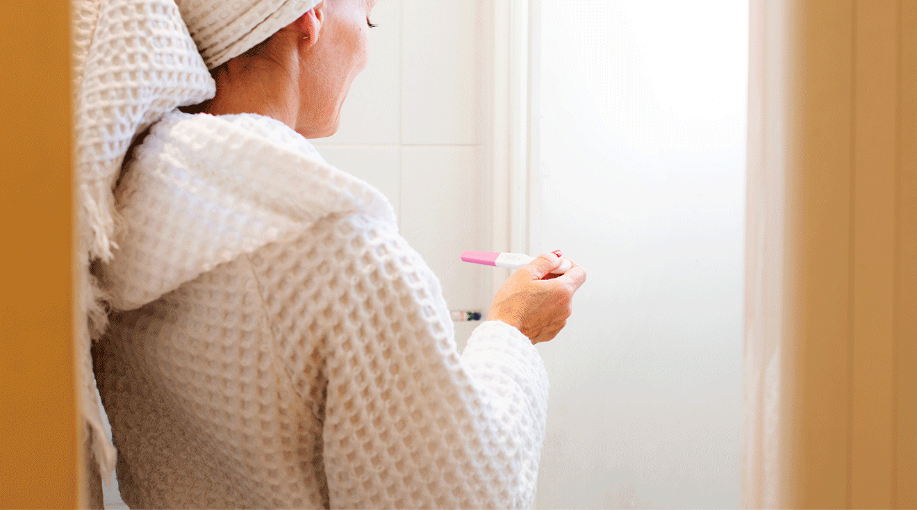 woman reading pregnant test in bath robe in bathroom