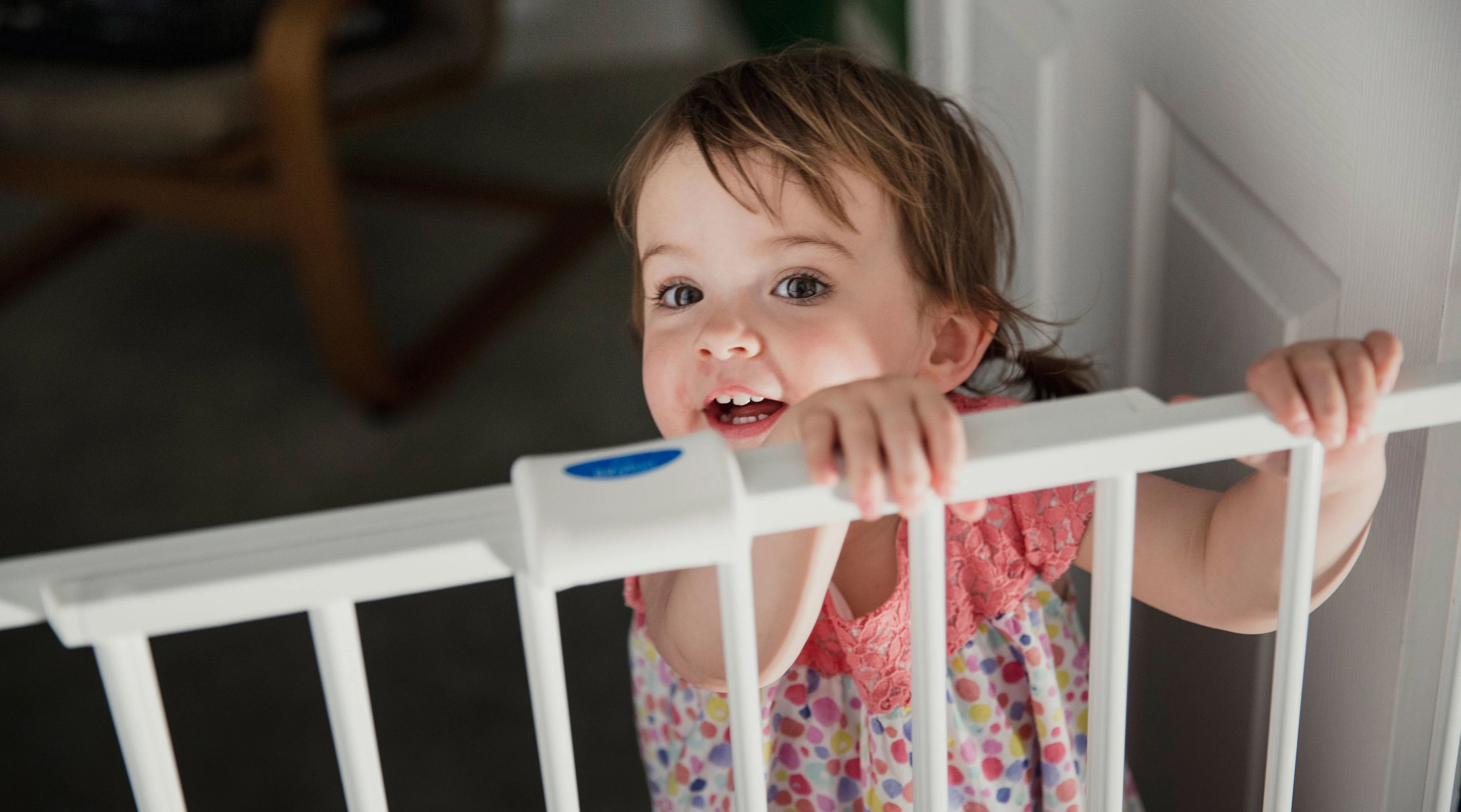 baby girl is walking and holding onto safety gate at home