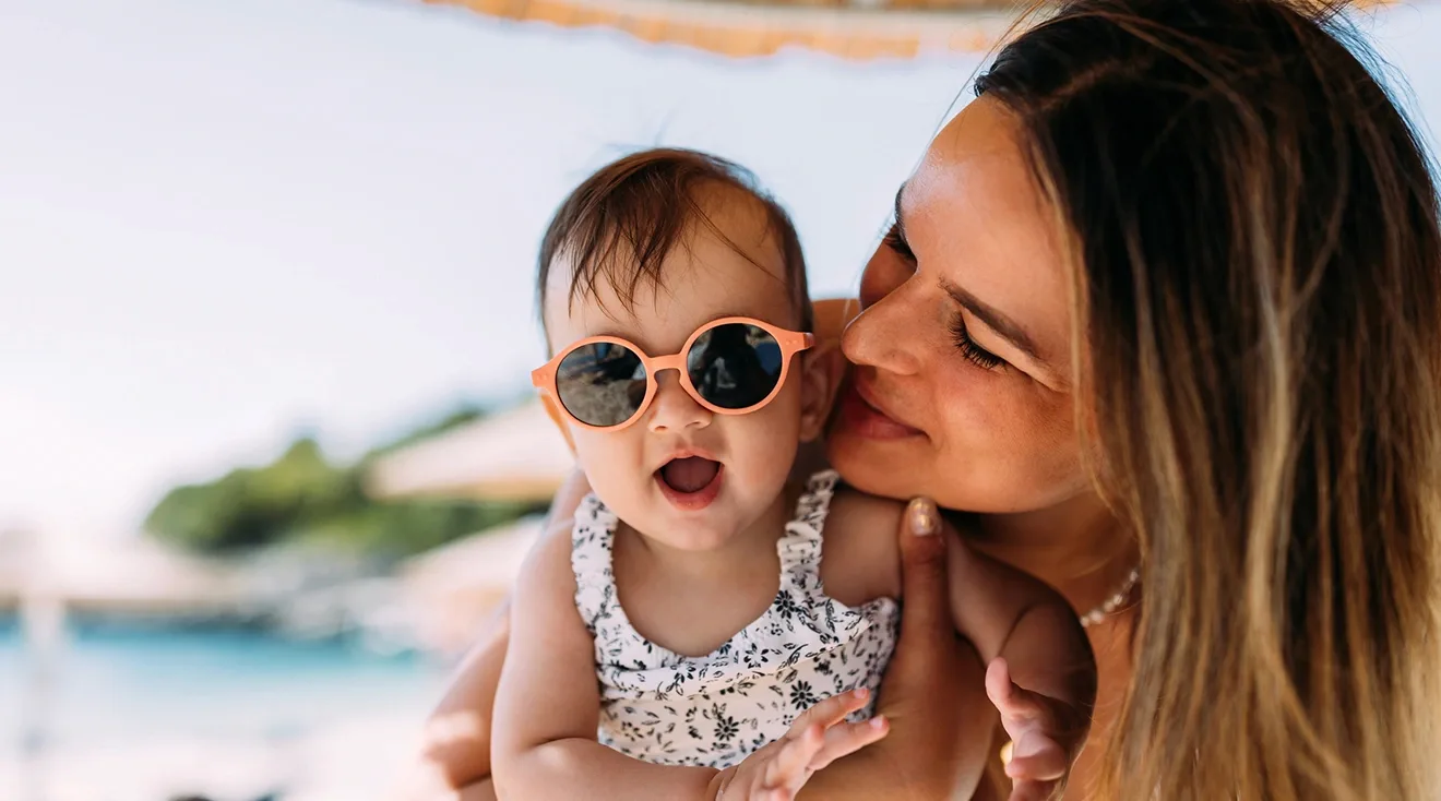 mother holding baby wearing sunglasses at the beach