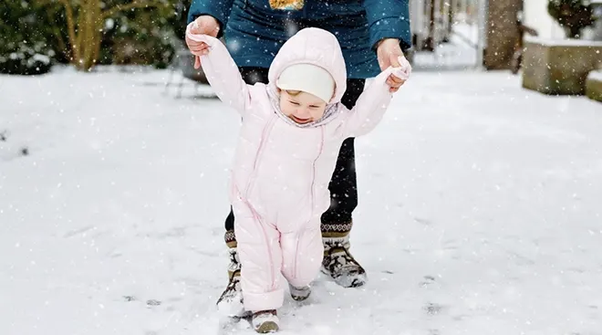mother helping baby walk in the snow