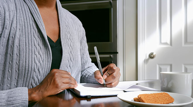 mid section of woman's hands sitting at table and writing in a journal