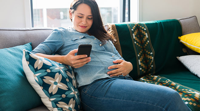pregnant woman at home on the couch on her phone
