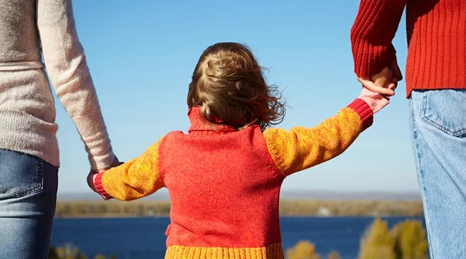 child holding both parent's hands while walking outside on a sunny day