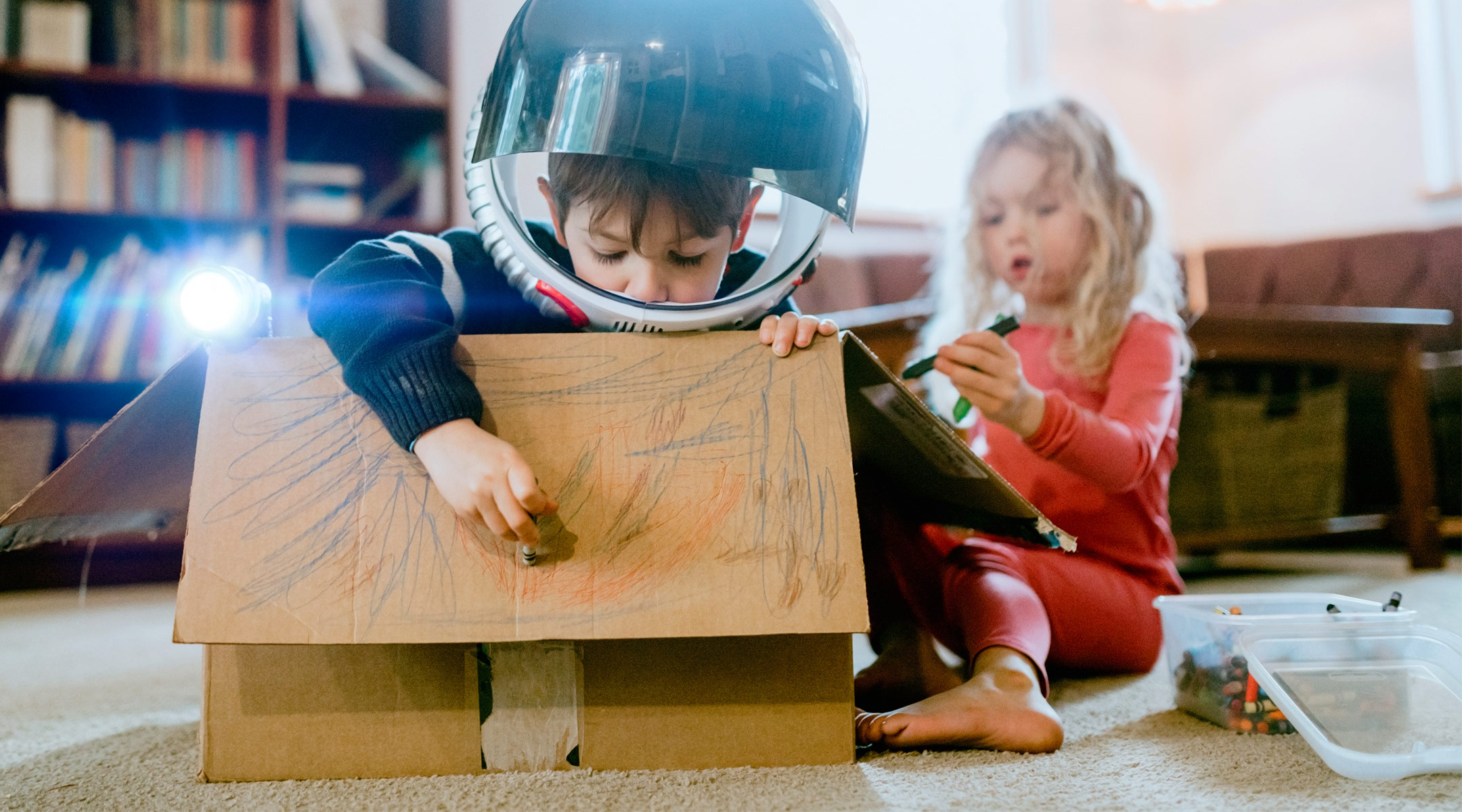 two children playing make space ship believe with a cardboard box