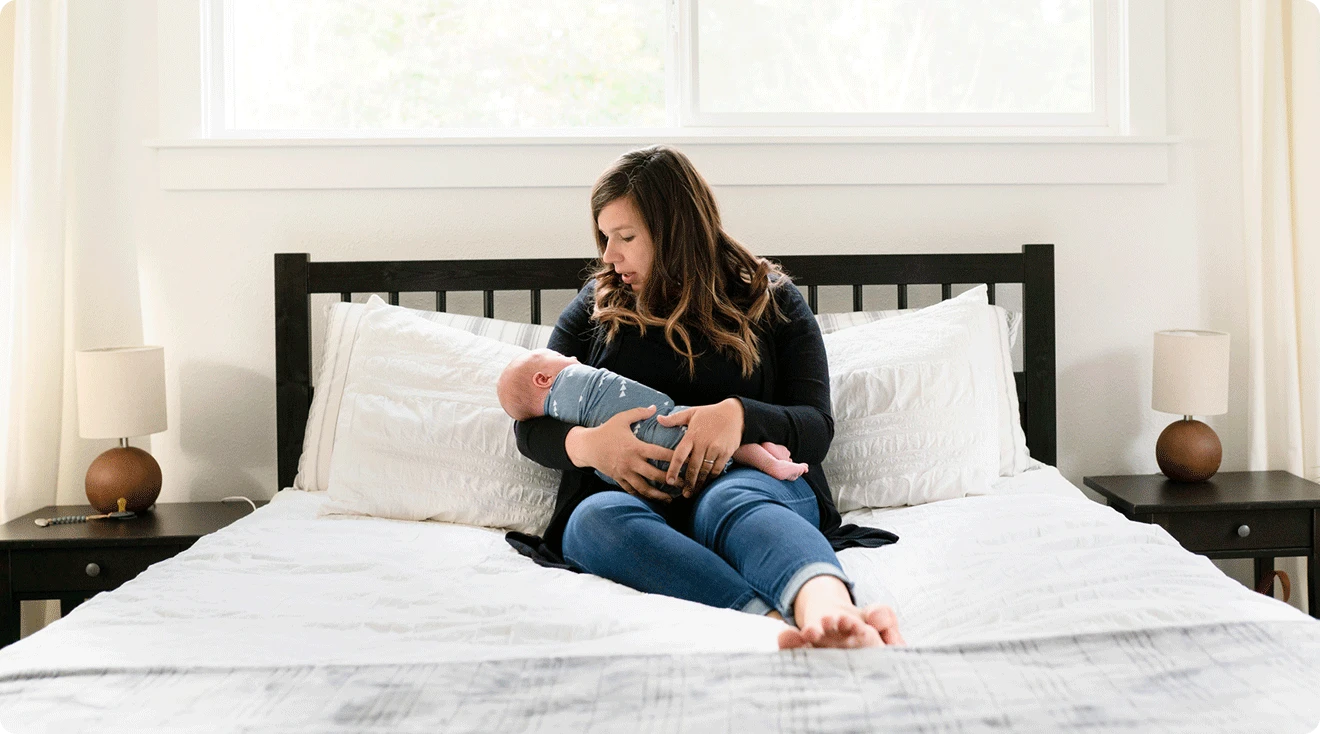 mom holding newborn baby on bed at home