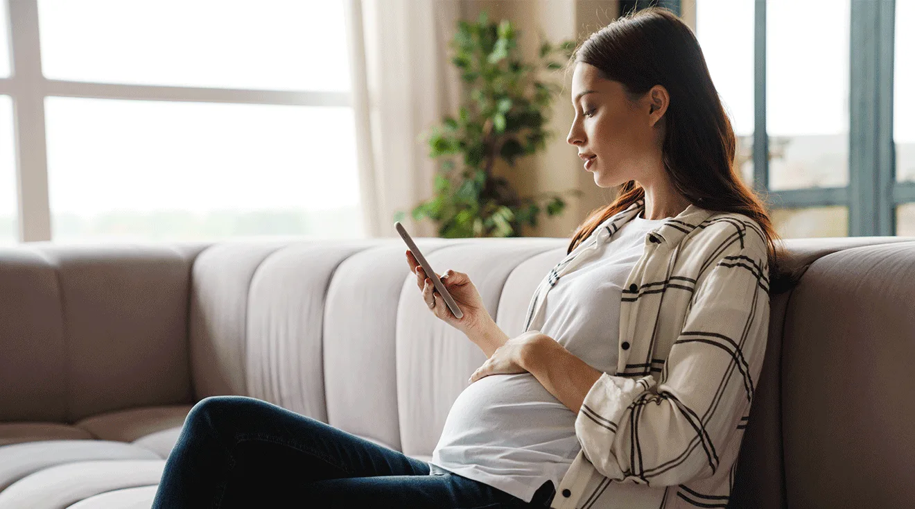 pregnant woman looking at phone while sitting on couch at home