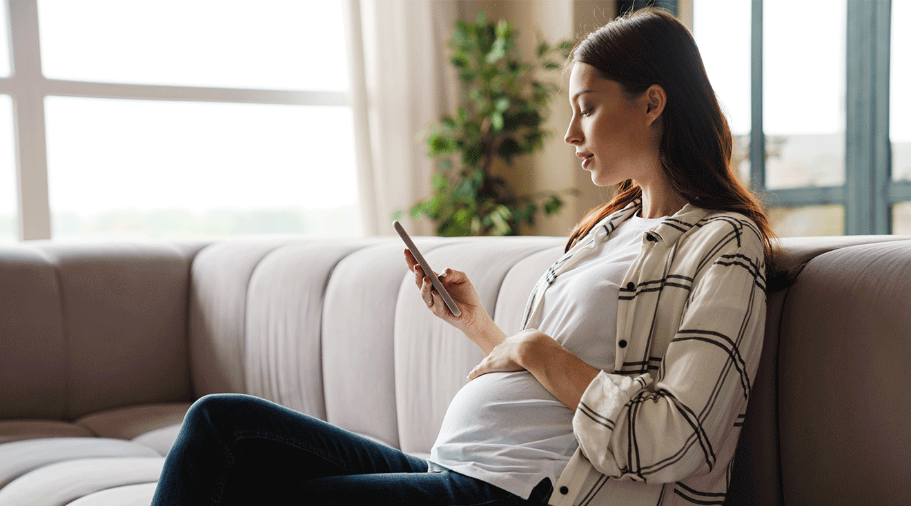pregnant woman looking at phone while sitting on couch at home