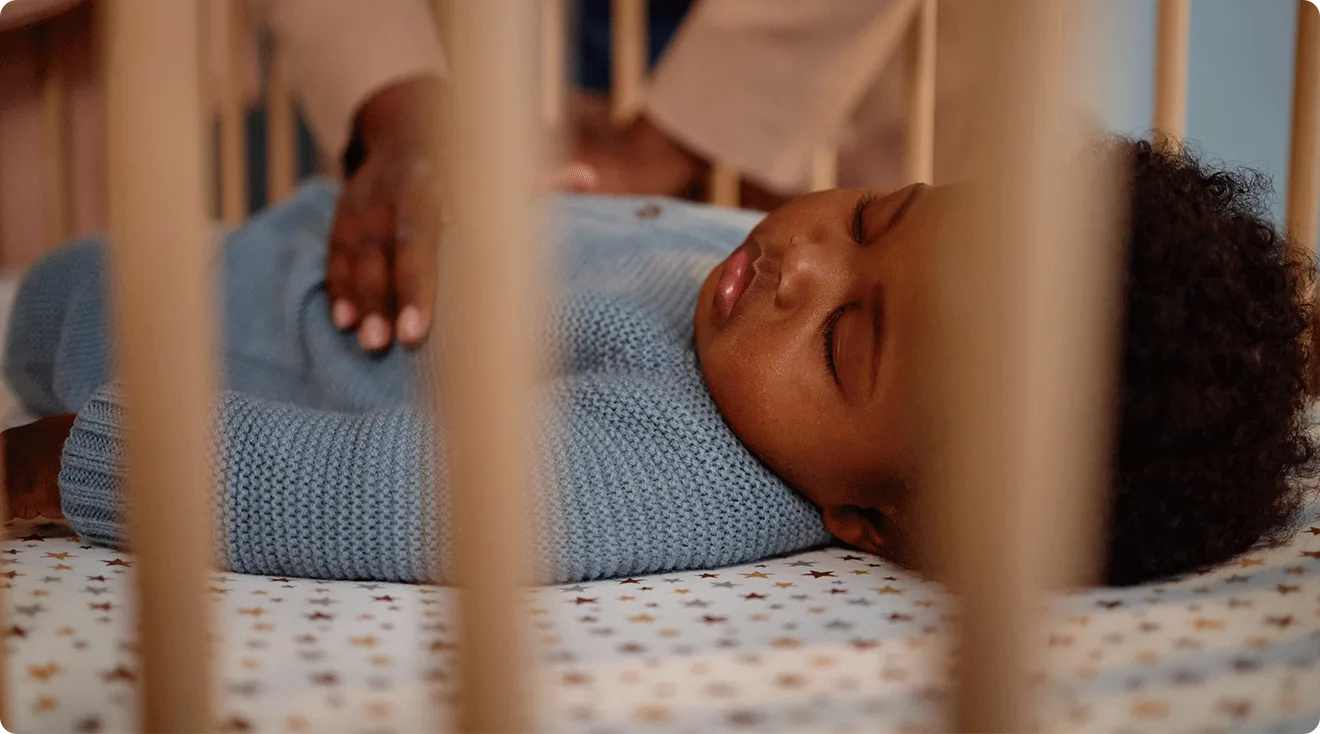 mom putting sleeping baby into crib