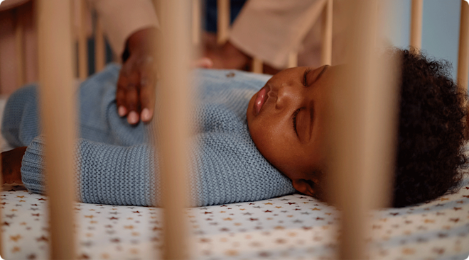 mom putting sleeping baby into crib