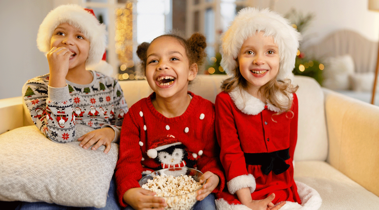 three kids watching christmas movies with popcorn on the couch at home