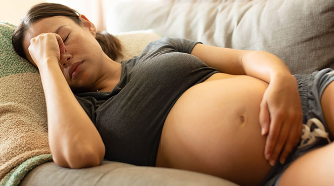 pregnant woman suffering from a migraine while laying on couch at home