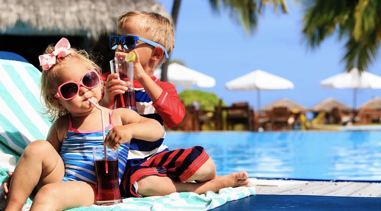 two young kids relaxing by the pool while on a tropical family vacation