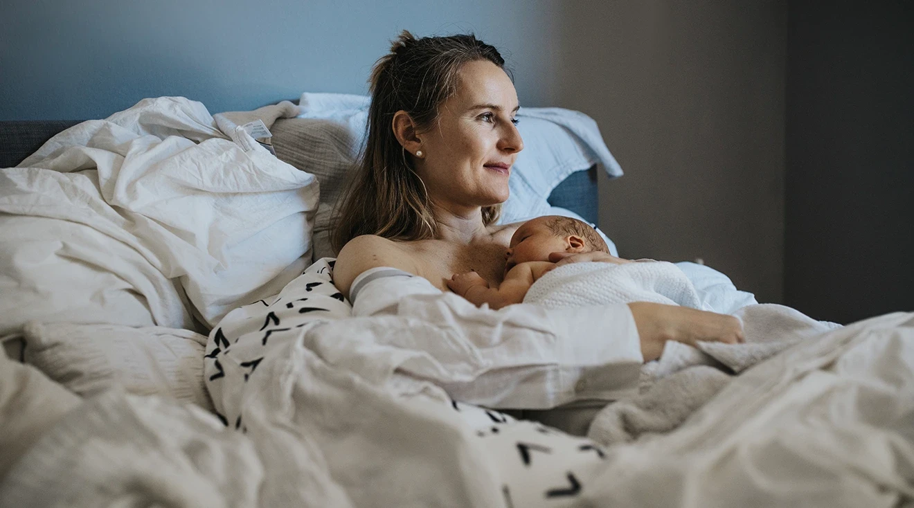 mother holding newborn baby in bed after home birth