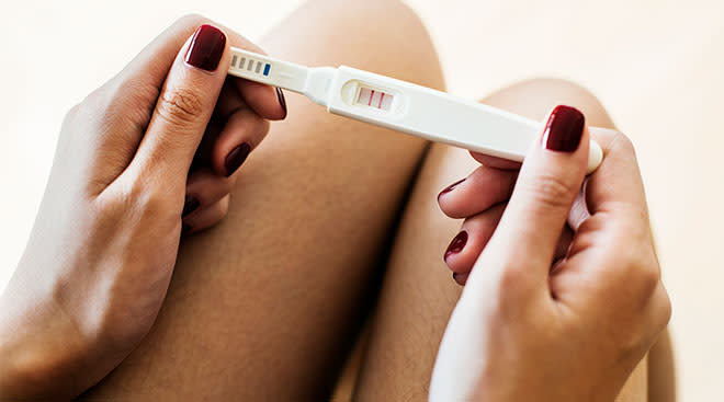 Close-up of woman's hands holding a positive pregnancy test near her legs. 