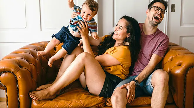 Family of three laughing and hanging out on the couch together. 