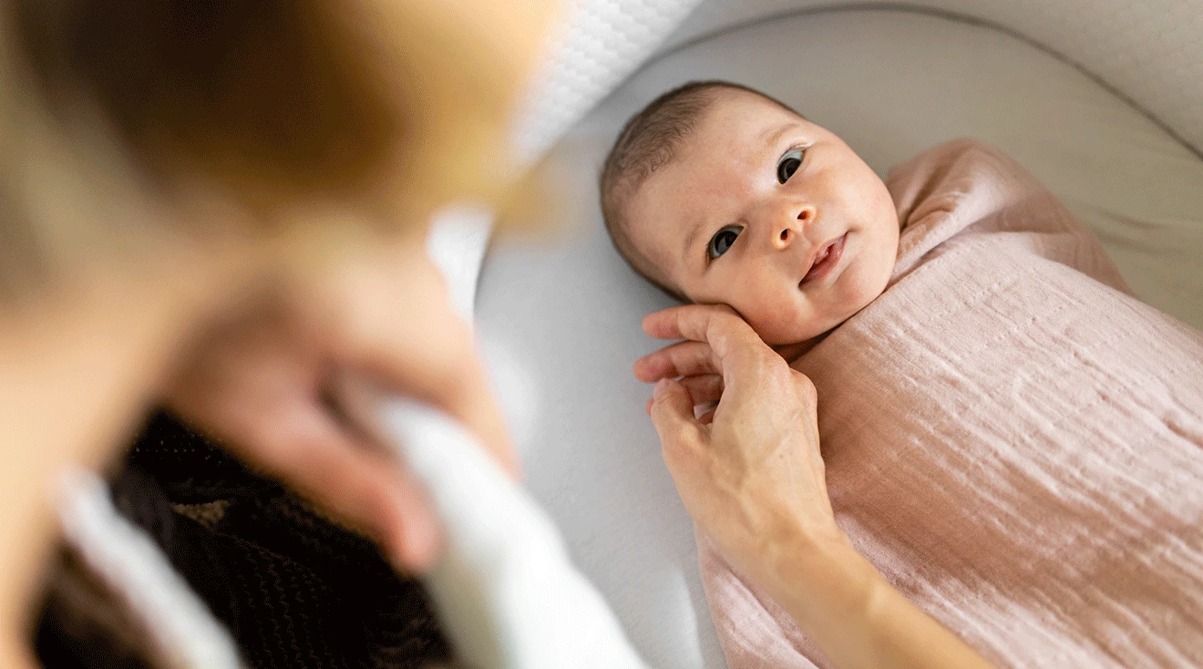 baby in bassinet looking at mother