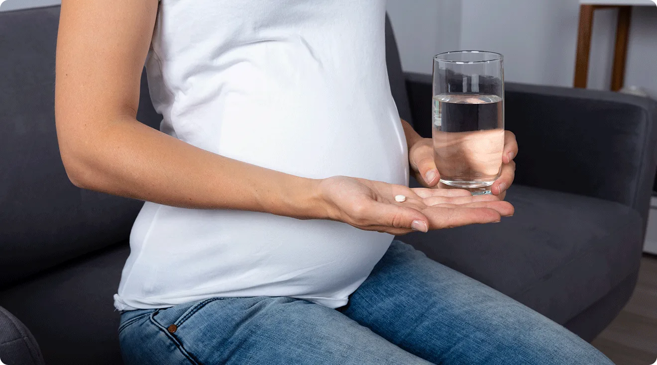 pregnant woman holding a white pill and glass of water