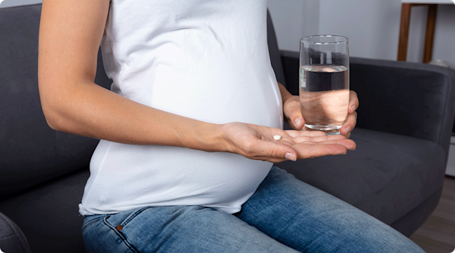 pregnant woman holding a white pill and glass of water