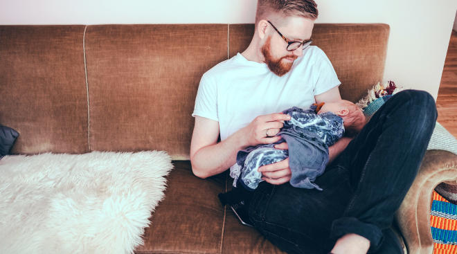 pensive dad holds and stares at his newborn baby at home