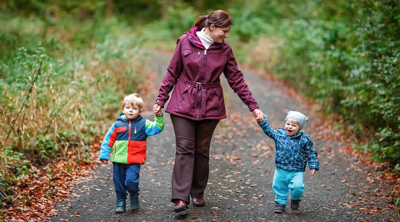 nanny holding hands with two children while walking outside
