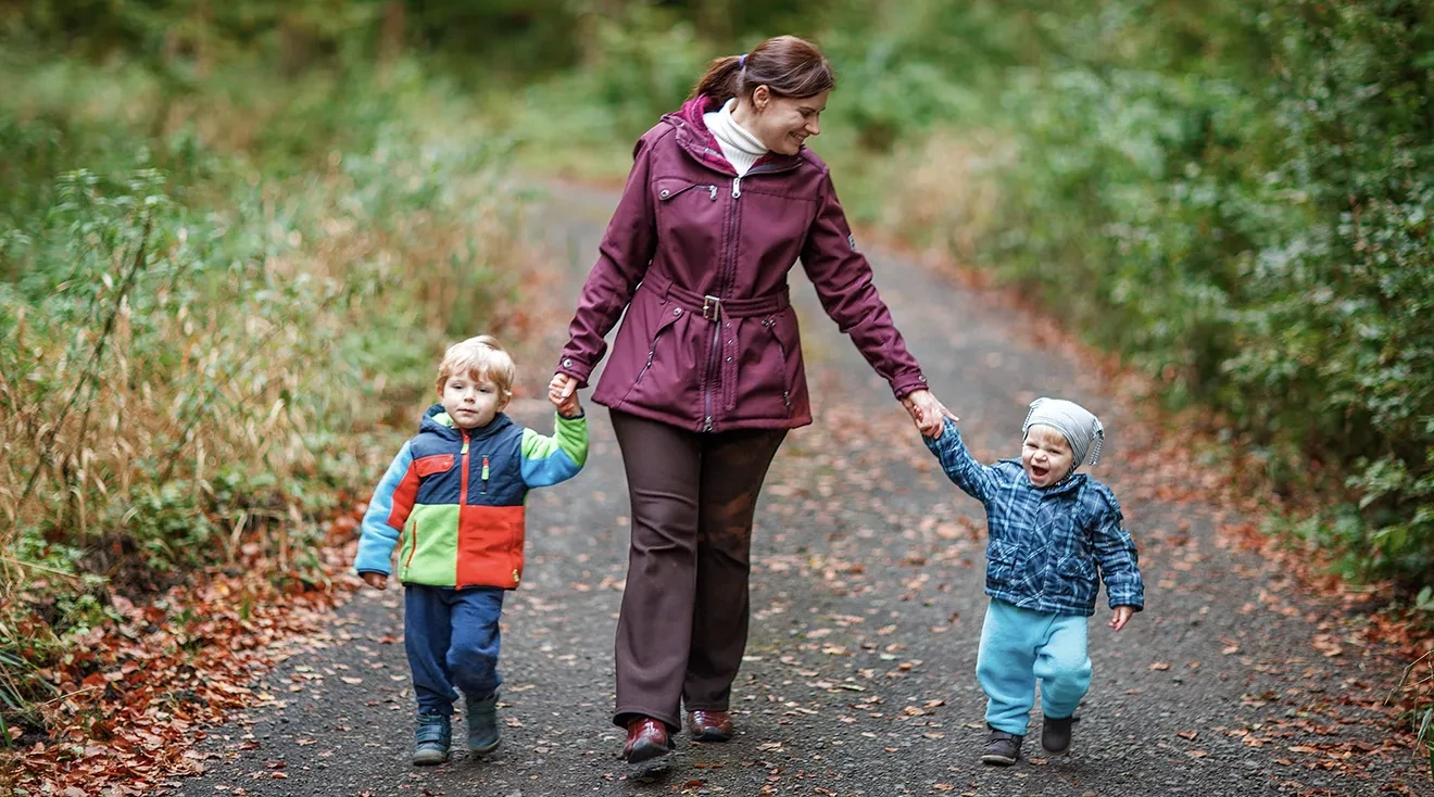 nanny holding hands with two children while walking outside