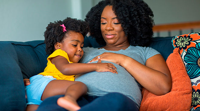 pregnant woman and her daughter smiling and touching her belly