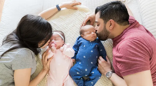 parents kissing newborn twin babies while in bed at home