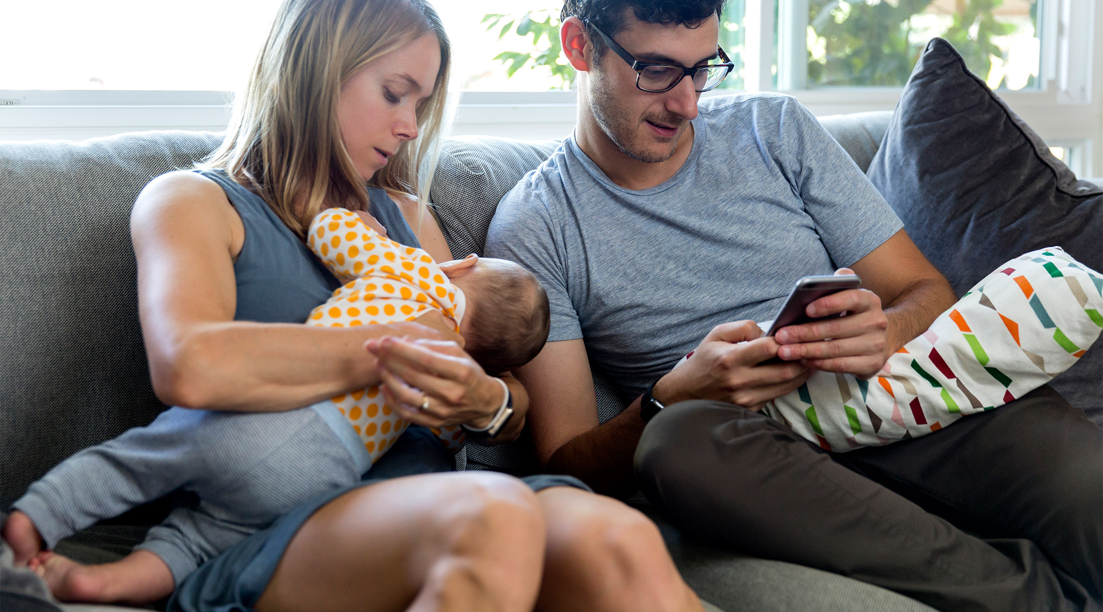 new mom breastfeeding baby while husband is on his phone