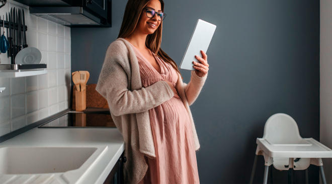 pregnant woman looking at tablet in her kitchen