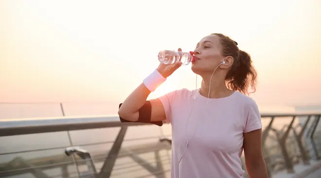 woman drinking water after workout outside during sunset
