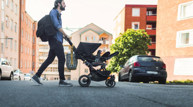 dad pushing baby stroller and carrying diaper bag