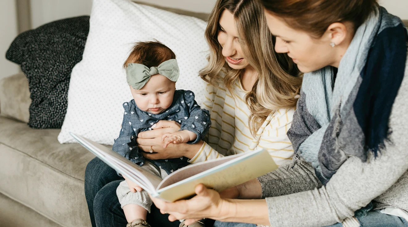 two moms reading to baby on the couch at home