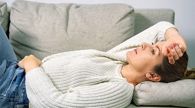 Woman laying on couch in pain, experiencing morning sickness.