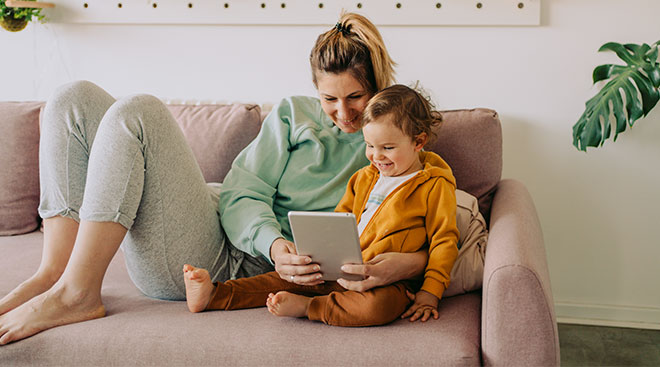 mother and young toddler sitting on the couch at home watching something on ipad