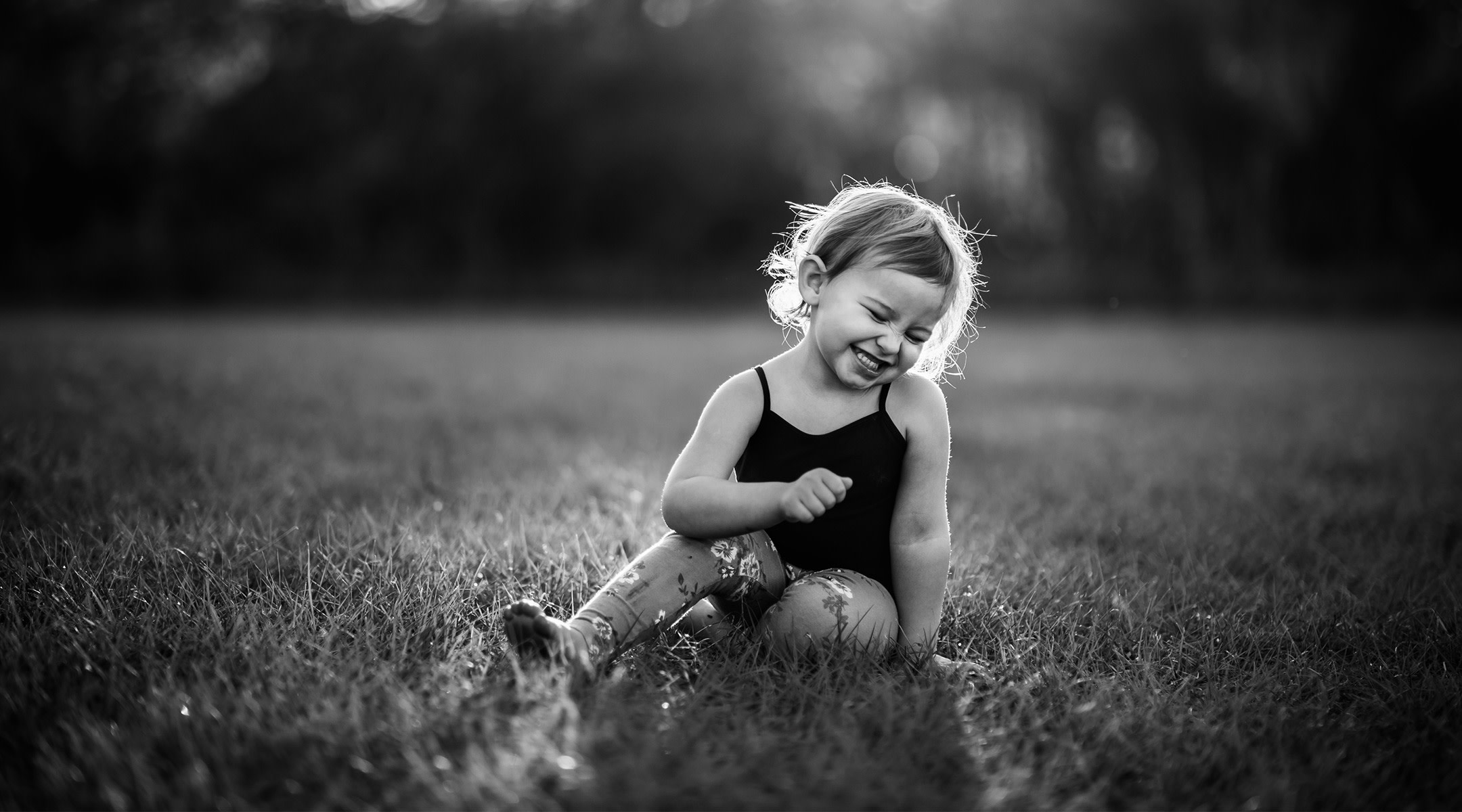 toddler girl sitting and candidly laughing outdoors