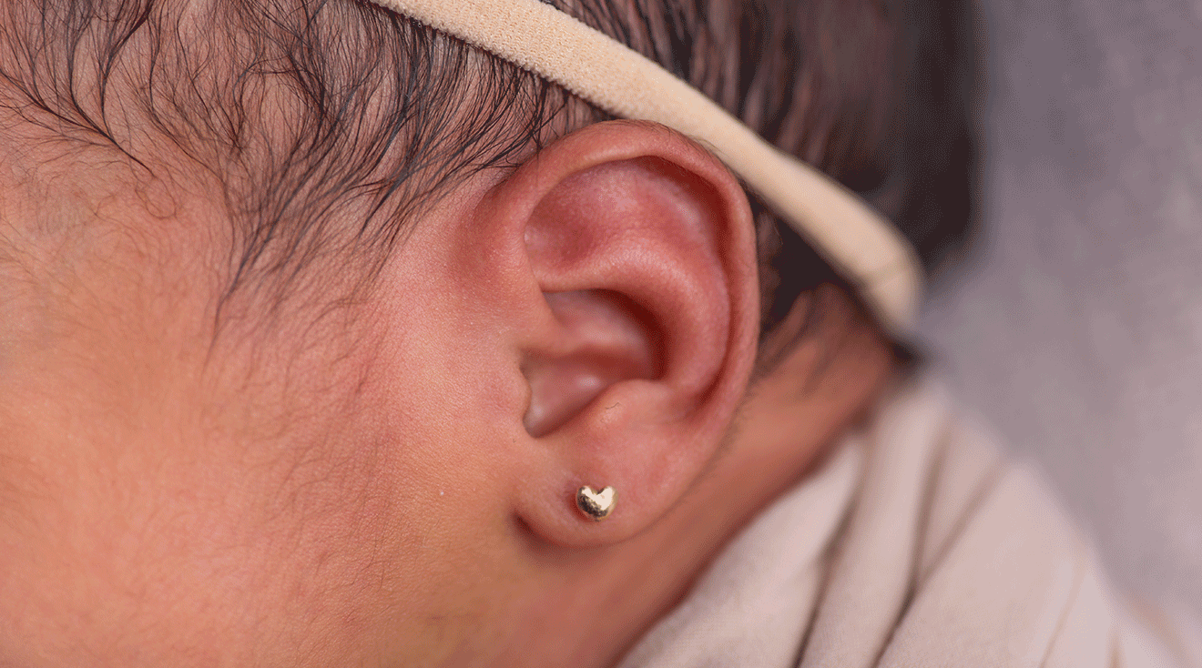 close up of newborn baby wearing earring in pierced ear