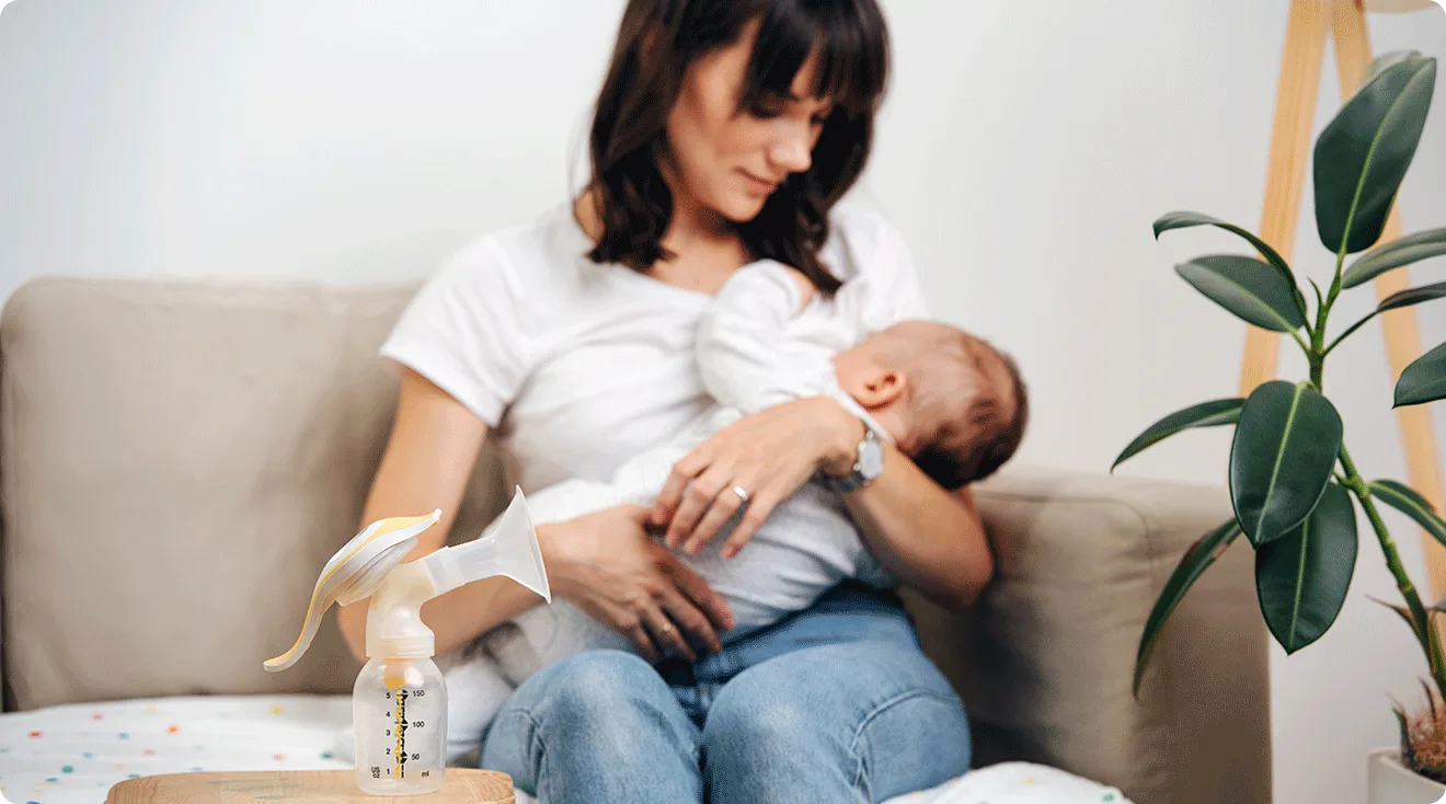 mom breastfeeding baby with breast pump on table nearby